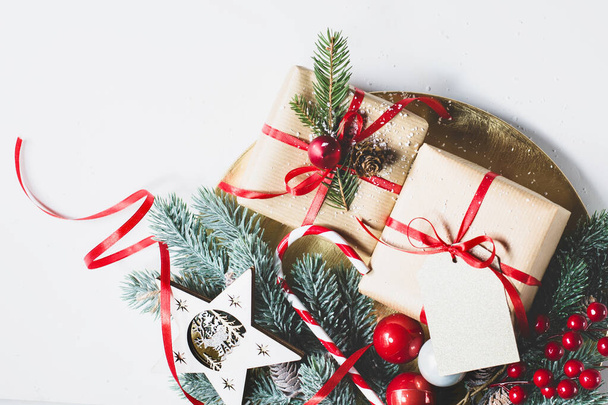 Piros szalagpapírba csomagolva, a karácsonyi ajándékok a lucfenyő ágakon vannak egy másik karácsonyi dekorációval együtt, könnyű háttérrel. Retro stílus. - Fotó, kép