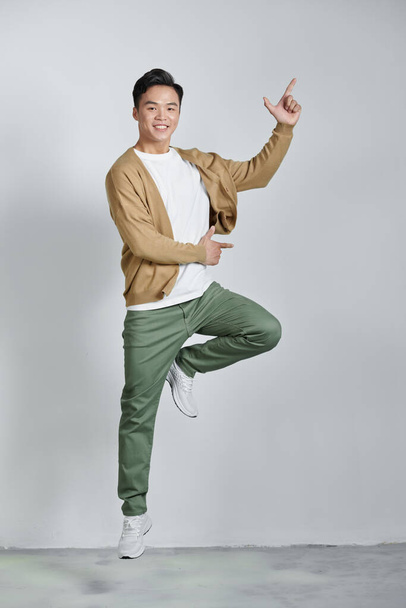 excited young Asian man jumping and pointing hand to empty space aside studio shot - Φωτογραφία, εικόνα
