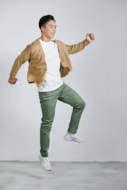 Mutlu, enerjik, genç Asyalı adam zıplıyor, bağırıyor ve yumruklarını sıkıyor. - Fotoğraf, Görsel