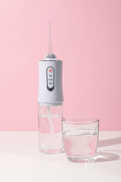 Irrigatore e bicchiere d'acqua sul tavolo su fondo rosa - Foto, immagini