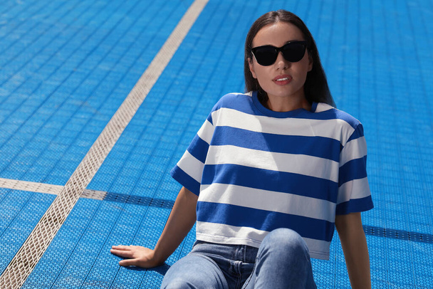 Beautiful woman in sunglasses on blue floor covering outdoors, space for text - Fotografie, Obrázek