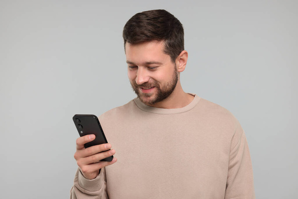 Happy man using smartphone on light grey background - Fotó, kép
