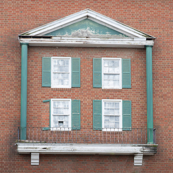 Quattro, vecchie finestre deteriorate con persiane verdi su un muro di mattoni esterno. Struttura unica che assomiglia a colonne, tetto e balcone. - Foto, immagini