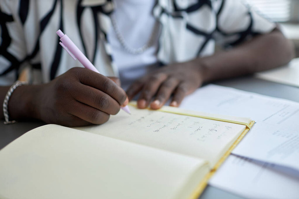 Skup się na ręce młodego Afroamerykanina, studenta robiącego notatki na pustym papge 'u z copybooków, zapisując odpowiedzi na pytania testowe. - Zdjęcie, obraz