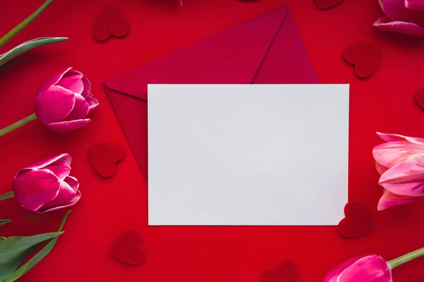 Empty white envelope copy space for your text or design with beautiful pink tulip bouquet on red background. Red small heart. Love romance Valentines day. Template mock up for holiday spring greeting - Photo, Image