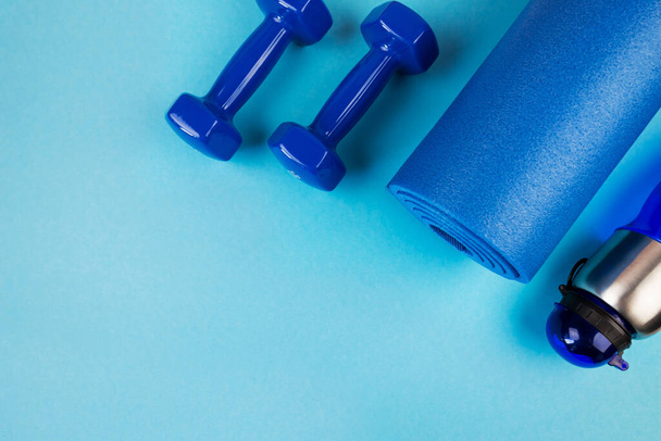 Vue du dessus du flacon d'haltère bleu et du tapis de fitness sur fond bleu avec espace de copie. - Photo, image