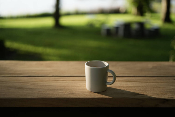 Λευκό φλιτζάνι καφέ σε καφέ ξύλινο πάγκο με φύλλα της φύσης φόντο - Φωτογραφία, εικόνα