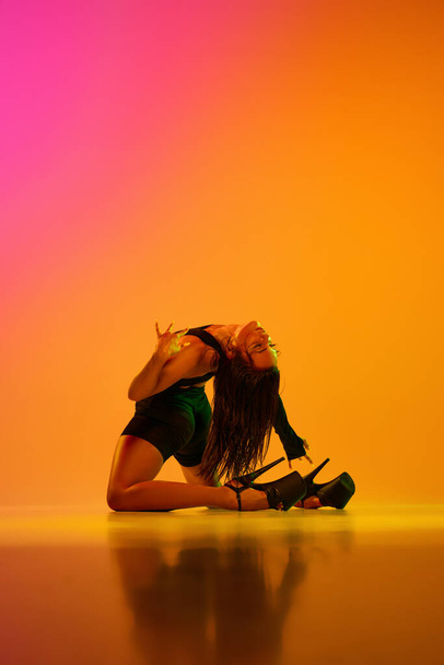 Портрет молодой девушки, танцовщицы на высоких каблуках, позирующей на полу над студийным фоном в неоновом цвете со смешанным освещением. Экспрессивное хобби. Концепция стиля современного танца, эстетики, хобби, творчества. - Фото, изображение