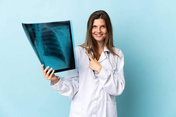 Junge Ärztin hält Röntgenbild über isoliertem Hintergrund und zeigt zur Seite, um ein Produkt zu präsentieren - Foto, Bild