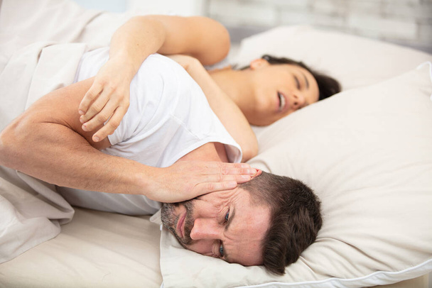 frustrated man covers ears with pillow cannot fall asleep - Foto, Imagen