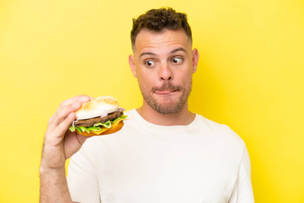 Nuori valkoihoinen mies, jolla on keltaisella pohjalla eristetty hampurilainen  - Valokuva, kuva