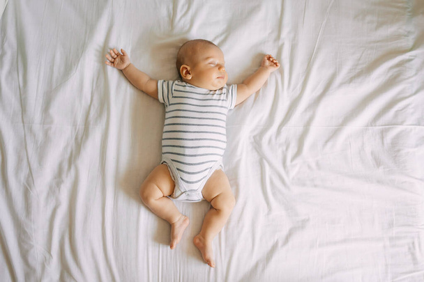 Top view sleeping newborn baby lies in a bed arms and legs outstretched. clean, fresh and cozy bedding sheets - Photo, Image