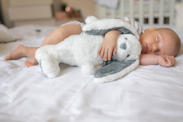 Yeni doğmuş bir bebek beyaz pamuklu yatakta uyur yumuşak bir oyuncakla, sağlıklı bir bebek uyur. - Fotoğraf, Görsel