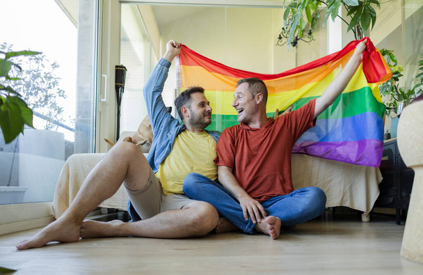 volwassen paar gay mannen met gay trots vlag thuis - Foto, afbeelding