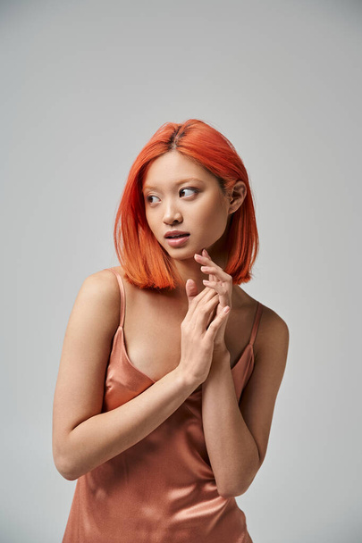 portrait of dreamy young asian woman with red hair posing in silk slip dress on grey background - Photo, Image