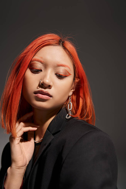 portré fiatal ázsiai nő vörös haj, orrpiercing és szemfesték pózol szürke - Fotó, kép