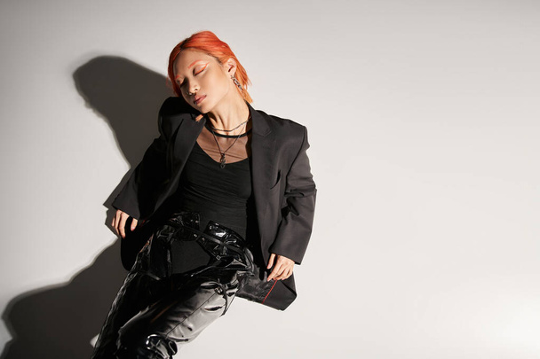 top view of asian woman with closed eyes and red hair posing in bold attire on grey background - Φωτογραφία, εικόνα