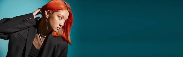 asian woman with red hair and nose piercing posing in oversized blazer on blue backdrop, banner - Photo, Image