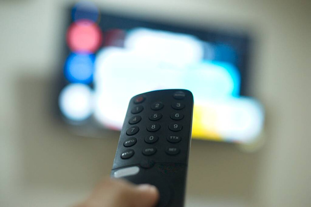 Hand mit TV-Fernbedienung, Umschalten von TV-Serien von Streaming-Service-Plattform. Die neue Art der Unterhaltung zu Hause. - Foto, Bild