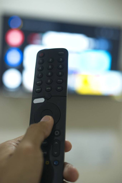 Hand mit TV-Fernbedienung, Umschalten von TV-Serien von Streaming-Service-Plattform. Die neue Art der Unterhaltung zu Hause. - Foto, Bild