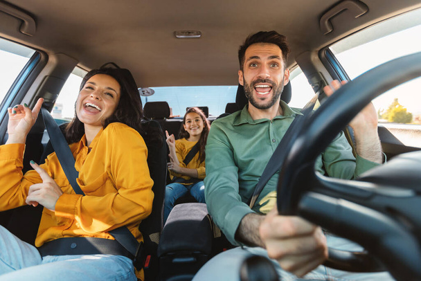 Nos vamos de vacaciones. Familia feliz de tres personas conduciendo en su automóvil, bailando con música y cantando su canción favorita, disfrutando viajar en coche - Foto, imagen