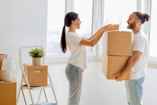 Happy young spouses packing boxes for moving, relocating to new apartment standing at home. Real esate rent, mortgage and ownership concept. Family millennial couple preparing to move house - Photo, Image