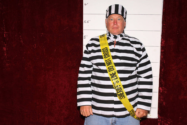 Photo Booth. Un homme porte un uniforme rayé en prison devant un Mugshot Chart de la police aka photo de réservation. - Photo, image