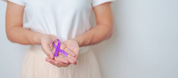 Женщина держит фиолетовую ленту от насилия, поджелудочной железы, пищевода, рака яичек, Альцгеймера, эпилепсии, волчанки, саркоидоза и фибромиалгии. Концепция Всемирного дня борьбы с раком - Фото, изображение