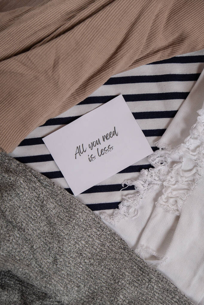 ALL YOU NEED IS LESS text on paper note on clothes assortment Second hand sustainable shopping. Capsule minimal wardrobe. Sustainable fashion overconsumption, conscious buying consumption, slow - Photo, Image