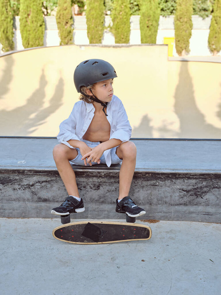 Pełne ciało małego dziecka w kasku ochronnym z longboardem na rampie w skate parku - Zdjęcie, obraz