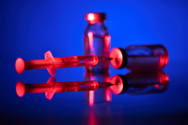 Nahaufnahme medizinischer Ampullen und Spritzen, die mit COVID19-Impfstoff gefüllt und für die Impfung in Neonlicht vorbereitet wurden - Foto, Bild