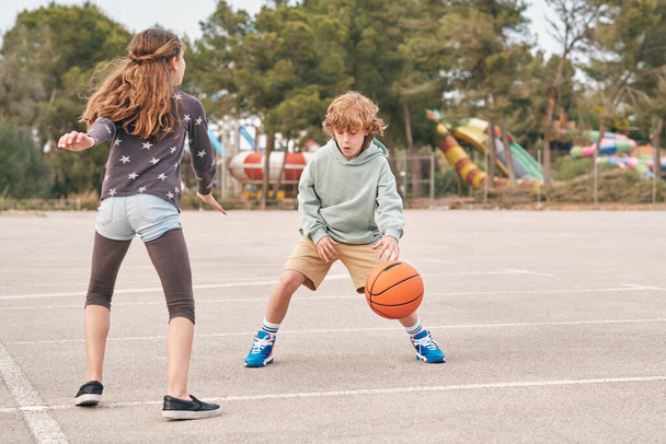 Teen boy and girl playing basketball on playground while entertaining together at weekend - Photo, Image