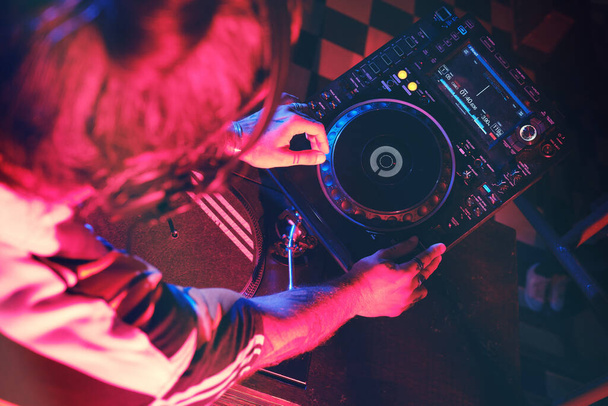 Van boven uit gewas anonieme getalenteerde DJ spelen lied op moderne CDJ-speler tijdens het werken in nachtclub met schemerige verlichting - Foto, afbeelding