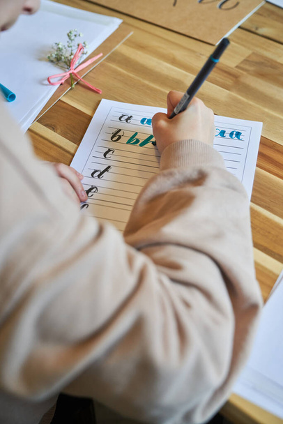 Зверху невизначена людина малює літери на паперовому аркуші, використовуючи барвистий маркер у творчій робочій області
 - Фото, зображення