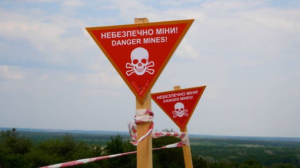 Sinais com a inscrição de aviso Perigo, minas e fitas de esgrima em frente ao assentamento. Áreas minadas em aldeias ucranianas. Guerra russo-ucraniana 2022-2023. O conceito de desminagem humanitária - Foto, Imagem