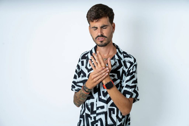 man with tattoo wearing summer shirt standing over isolated white background suffering pain on hands and fingers, arthritis inflammation - Photo, Image