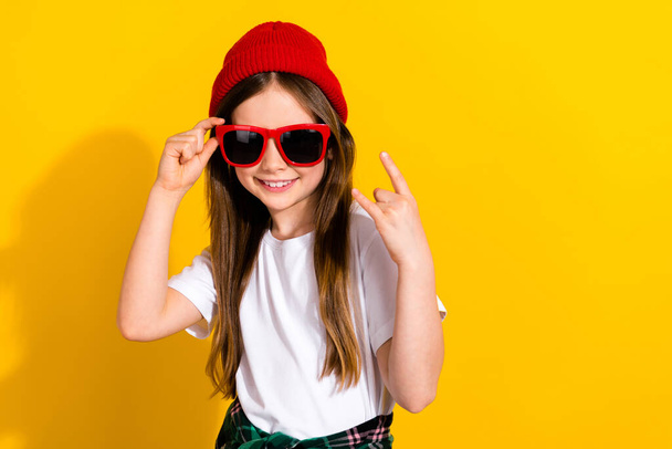 Photo portrait of charming little girl sunglass showing rock gesture sign dressed stylish white garment isolated on yellow color background. - Фото, изображение