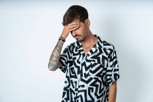 A very upset and lonely man with tattoo wearing summer shirt standing over isolated white background crying - Photo, Image