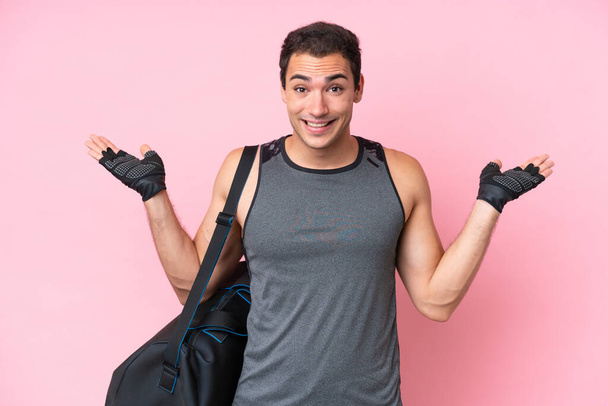 Joven hombre caucásico deporte con bolsa de deporte aislado sobre fondo rosa con expresión facial impactada - Foto, imagen