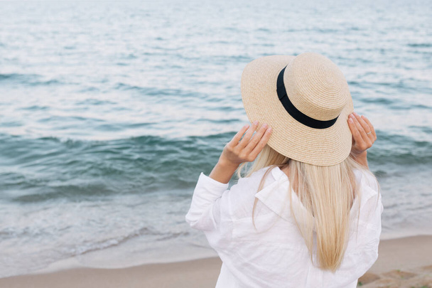 Jolie femme élégante blonde tannée mince dans un chapeau de paille posant sur une plage tropicale paradisiaque. - Photo, image