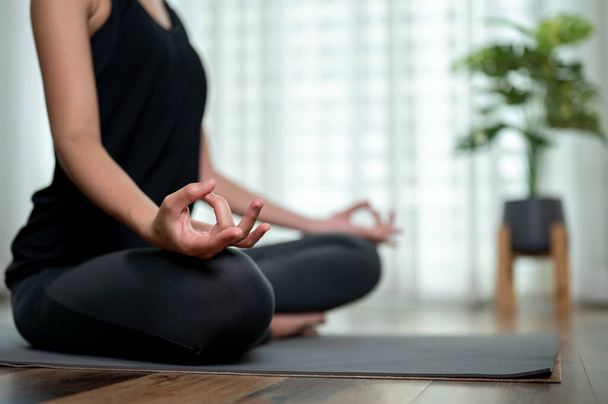Close-up achteraanzicht van een gezonde, sportieve vrouw die thuis yoga beoefent, zittend in een lotushouding op een yogamat in de woonkamer. - Foto, afbeelding