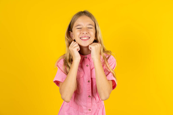 dívka v růžové bundě přes žluté pozadí se radostně usmívá, představuje si něco příjemného, kopírovací prostor. Příjemný koncept emocí. - Fotografie, Obrázek