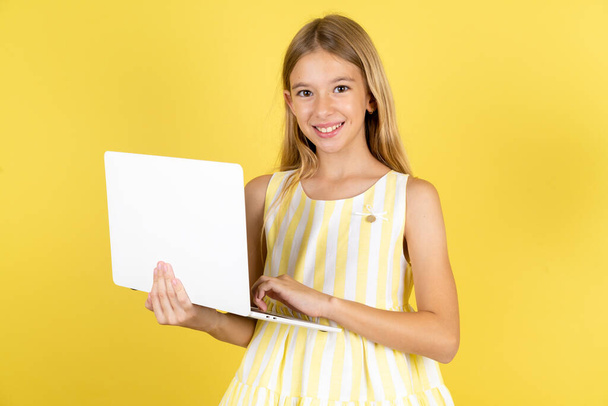 Adorabile ragazza che indossa abito giallo su sfondo giallo che tiene dispositivo moderno - Foto, immagini