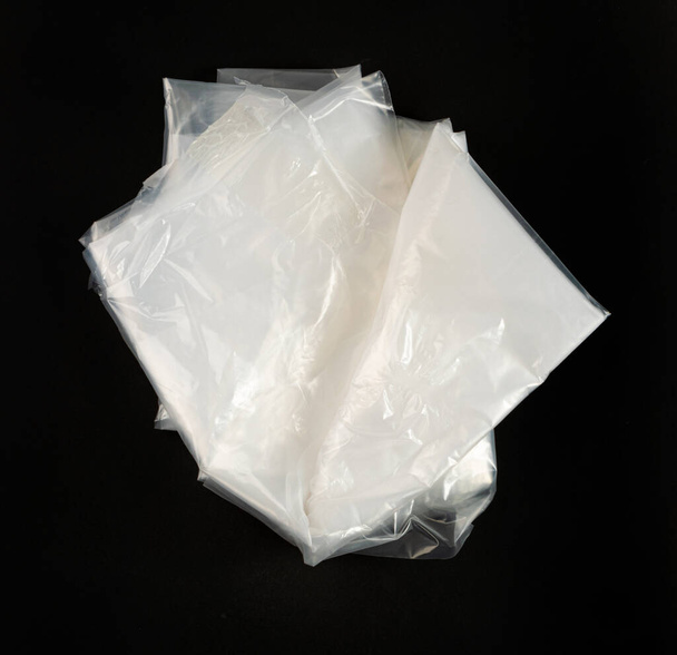 Gefaltete weiße Plastiktüten auf schwarzem Hintergrund, zerknitterte Plastiktüte nach dem Einkaufen, Cellophan Verpackungsmüll, gebrauchte zerknitterte Einwegtasche - Foto, Bild