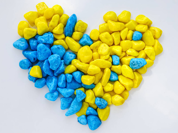 Renkli mavi ve sarı taşlardan yapılmış bir kalp. Ukrayna bayrağı renginde bir kalp. Mavi ve sarı renk. Dekorasyon malzemesi. Romantik kartpostal. Sevgililer Günü. Beyaz bir arka planda kalp. - Fotoğraf, Görsel