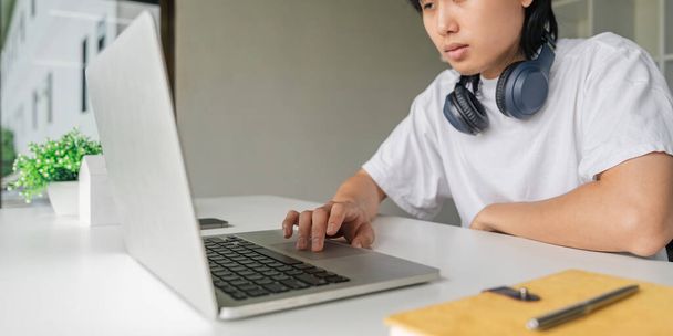 Azji młody człowiek za pomocą laptopa podczas relaksu siedzi przy stole. - Zdjęcie, obraz