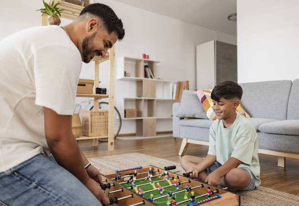 Ισπανόφωνος πατέρας με το γιο του στο σπίτι να παίζει ποδοσφαιράκι. - Φωτογραφία, εικόνα