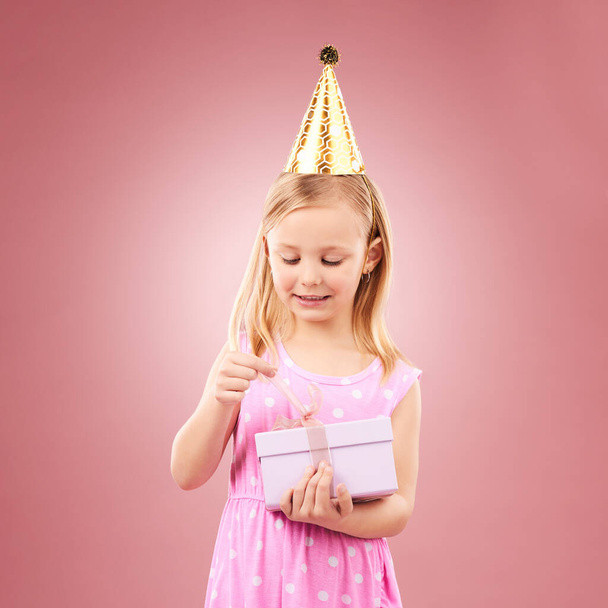 Подарок, шляпа и ребенок открыть подарочную коробку для праздничной вечеринки или счастливого праздника. Возбужденная девушка на розовом фоне для сюрпризов, подарков приз или отпраздновать победу на мероприятии с лентой и радостью. - Фото, изображение