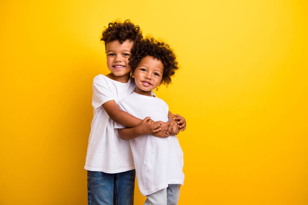 Portrait of two adorable cute kids toothy smile cuddle support empty space ad isolated on yellow color background. - Фото, зображення
