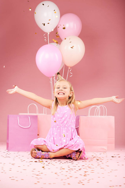 Balões, aniversário e retrato de menina animada em fundo rosa para festa, celebração e evento. Feliz, confete e criança com braços abertos para presentes, caixa de presente e decoração em estúdio. - Foto, Imagem